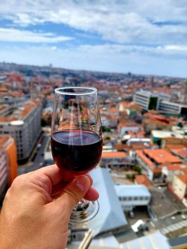 Sklenička portského vína Ruby držená v ruce s výhledem na město Porto